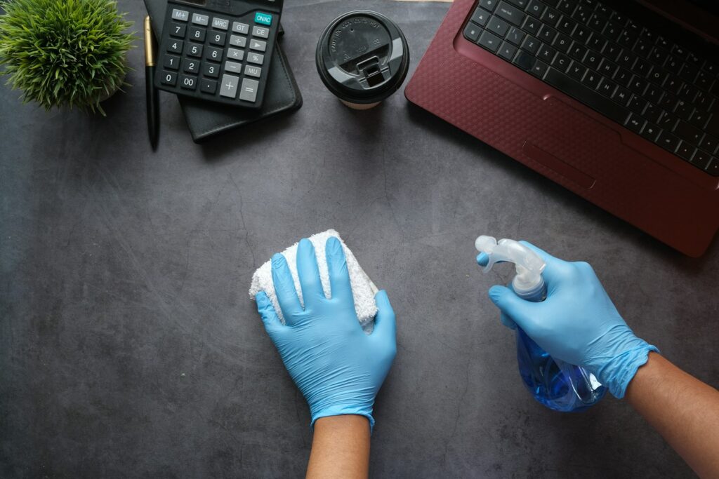 Hände in Handschuhen wischen einen Tisch mit Tuch und Sprühflasche